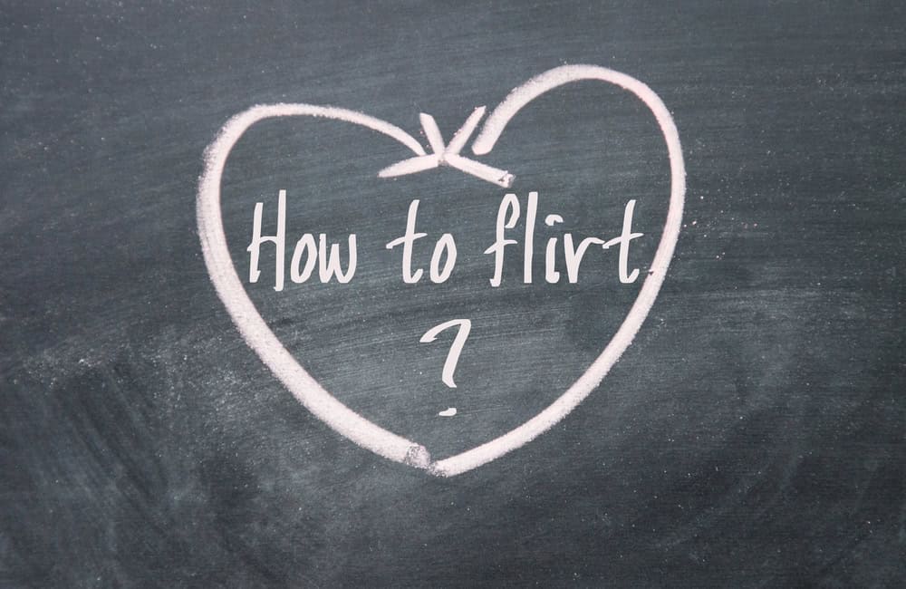 The phrase "How to flirt?" is written inside a heart drawn with pink chalk on a blackboard-a charming nod to flirting without pressure.